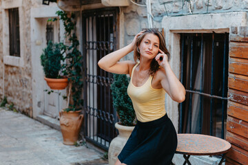 Girl Tourist Walking Through Ancient Narrow Street On A Beautiful Summer Day In MEDITERRANEAN MEDIEVAL CITY, OLD TOWN BUDVA, MONTENEGRO. Young Beautiful Cheerful Woman Walking On Old Street At