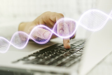 Double exposure of creative DNA hologram and hands typing on laptop on background. Bio Engineering and DNA Research concept