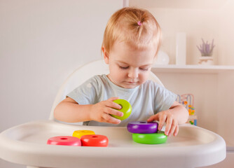 Little child plays with colorful wood toys pyramid sitting on highchair. Baby game. Games for early development