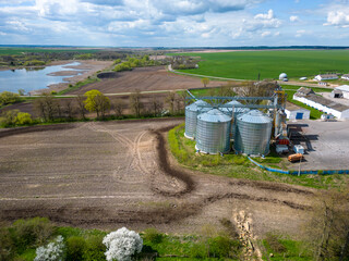 Obraz premium Flying a drone over silver silos on agro manufacturing plant for processing drying cleaning and storage of agricultural products, flour, cereals and grain. Large iron barrels of grain. aerial view