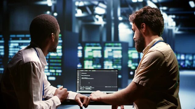 IT developers team writing server script code in data center on laptop terminal. Teamworking programmers doing maintenance work in high tech facility updating rigs software