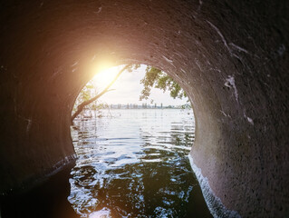 Light at end of round flooded sewer tunnel. Exit from sewer system