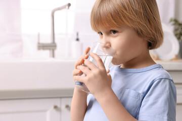 Cute little boy drinking fresh water from glass at home. Space for text