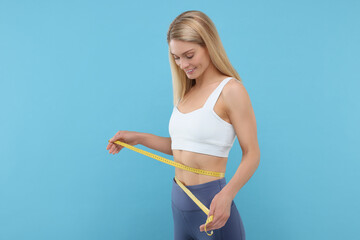 Slim woman measuring waist with tape on light blue background. Weight loss