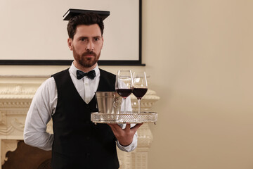 Man with tray and book on head practicing good posture indoors, space for text. Professional butler courses