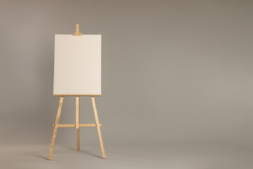 Wooden easel with blank canvas on grey background. Space for text