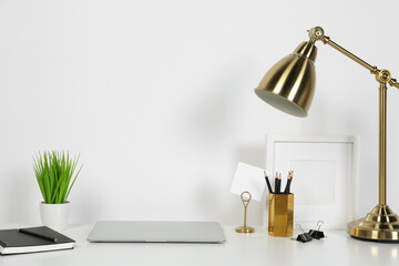 Cozy workspace with laptop, lamp and stationery on white desk at home