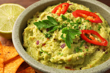 Bowl of delicious guacamole, lime and tortilla chips, closeup