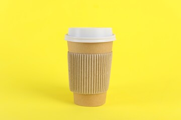 Paper cup with plastic lid on yellow background. Coffee to go