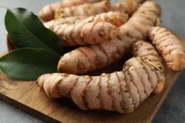 Many raw turmeric roots and green leaves on grey table, closeup