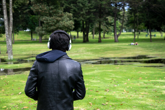 Young man on his back in leather jacket and headphones. Boy enjoying the music while he appreciates the natural landscape of wetlands and trees