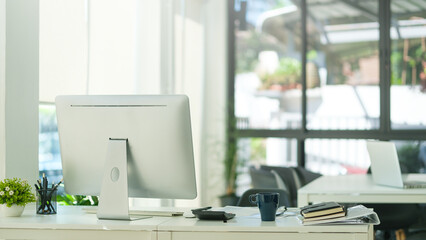 Modern workplace with computer monitor, coffee cup and office supplies on white table.
