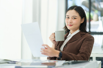Successful corporate CEO woman in stylish suit sitting at modern workplace and looking confidently to camera.