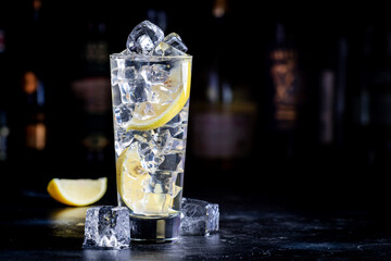 Vodka tonic alcoholic cocktail drink with cold vodka, lemon juice, bitter tonic and ice cubes. Black background, bar counter with bottles