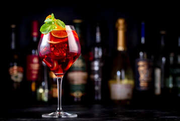 Red sangria summer alcoholic drink with red spanish wine, peach, plum, orange, lime and ice. Black bar counter background, steel bar tools and bottles
