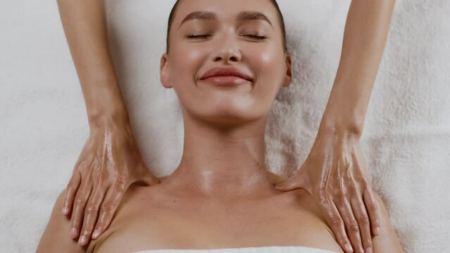 Portrait of young satisfied woman enjoying massage at spa salon, beautician massaging her shoulders and neckline