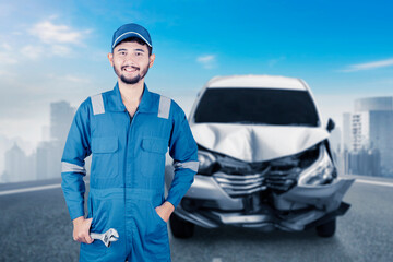Smiling mechanic over blurred front of silver car get damaged by accident on the road
