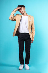 Full length image of young man in casual blazer touching his head while standing over blue background 