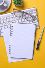 Vertical image of office desk with wireless keyboard, pen, notebook, glasses and succulent with blank page for text.