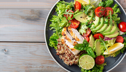 Healthy salad plate with quinoa, cherry tomatoes, chicken, avocado, lime and mixed greens, lettuce, parsley on wooden background top view. Food and health. Superfood meal.