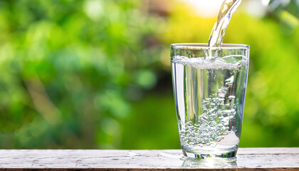 Drink water pouring in to glass over sunlight and natural green background