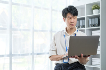 Handsome young asian man working on laptop computer at contemporary office.