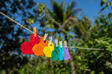Varal de corações de origami coloridos com as cores do arco-íris e presos por mini pregadores de...
