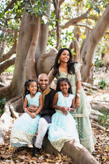 beautiful indian family sisters smiling with a bindi and traditional sari dress and kurta sitting on a tree