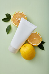 A white plastic tube for beauty cosmetics, mockup for face creams and cleansers with lemon extract ingredients. Advertising photo for natural organic cosmetics. Lemon and leaves on pastel background.