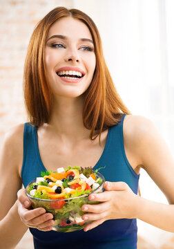 Image of happy amazed, smiling woman holding greece salad with cheese, indoor. Beautiful girl in casual blue dress - keto dieting, weight loss, healthy eating concept.
