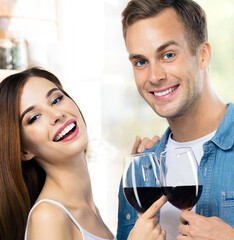 Attractive smiling young couple drinking redwine. Portrait image of caucasian models with red wine glasses in love concept. Man and woman posing together indoor. Square composition.