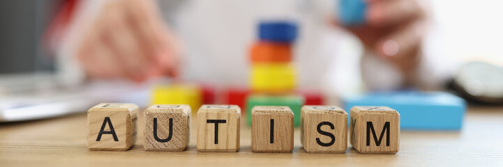 Word autism assembled from wooden blocks close-up and psychiatrist doctor with colored blocks.