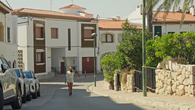 A woman strolling along a street lined with parked cars in Terragona