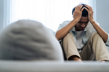 Obraz premium Asian young upset depressed man sitting alone in living room at home. 