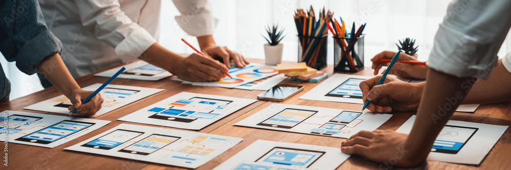 Poster Panorama shot of front-end developer team brainstorming UI and UX designs for mobile app on paper wireframe interface. User interface development team planning for user-friendly UI design. Scrutinize