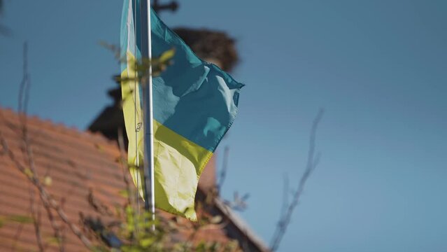 Ukrainian flag flatters in the wind. The stork nest and a cross on the church roof are in the background.