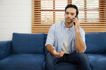 Fototapeta premium young handsome man sitting on sofa and talking by smartphone at home