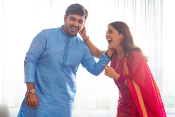 Sibling lovingly pulling each other's ear while celebrating Raksha Bandhan