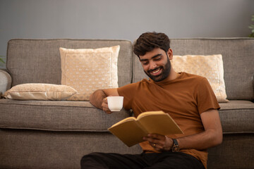 Smiling young man drinking tea while relaxing on sofa in living room