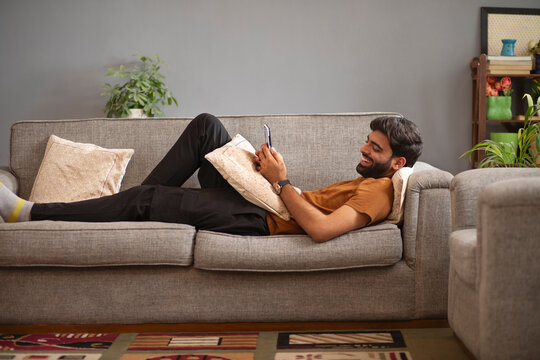 Young man using mobile phone while relaxing on sofa in living room