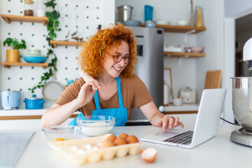Obraz na płótnie Canvas Professional beautiful happy young woman is blogging for her kitchen channel about healthy living in the kitchen of her home and looking on camera on a laptop