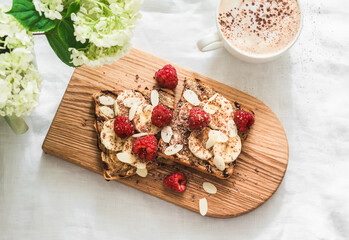 Delicious beautiful breakfast, snack, dessert - toast with peanut paste, banana, raspberry and chocolate, cappuccino, bouquet of hydrangeas on a white background, top view