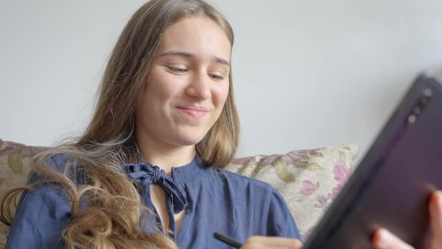 Camera footage, girl relaxing on sofa, using smart pen to write on tablet