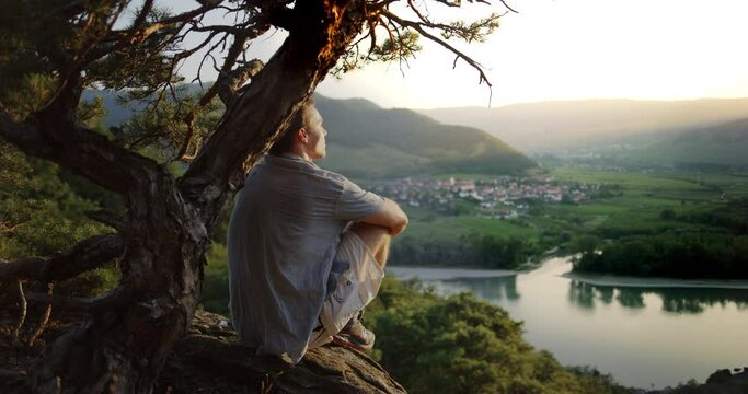 male looking at the sunset under a tree, mountain landscape background, golden hour river danube valley, overview, looking out, peaceful, detox, digital detox, outdoor nature, detox.