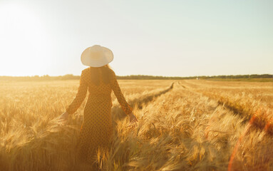 Beautiful young woman walks across the field and touches rye with her hand. Girl in the rays of the sunset. Freedom and happiness concept.
