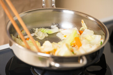 フライパンで野菜炒めを作る若い男性