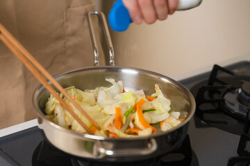 フライパンで野菜炒めを作る若い男性