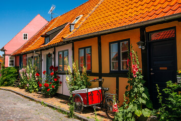 Yellow house and hollyhocks in Rønne, Bornholm Island in Denmark with bike and cart. - obrazy, fototapety, plakaty