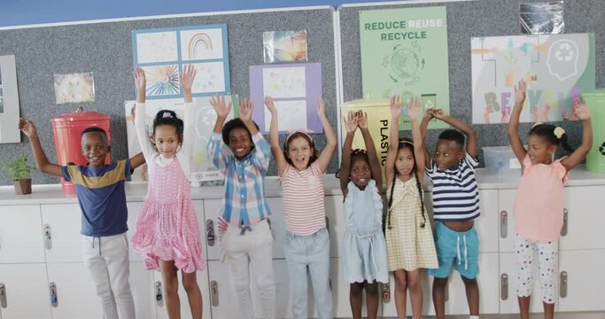 Portrait of happy diverse schoolchildren raising hands over ecology texts at elementary school