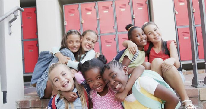 Portrait of happy diverse schoolgirls embracing each other at school lockers at elementary school